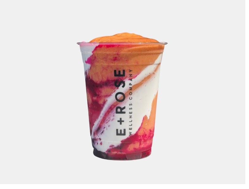 Layered orange and dragon fruit smoothie swirl in an E+ROSE branded cup